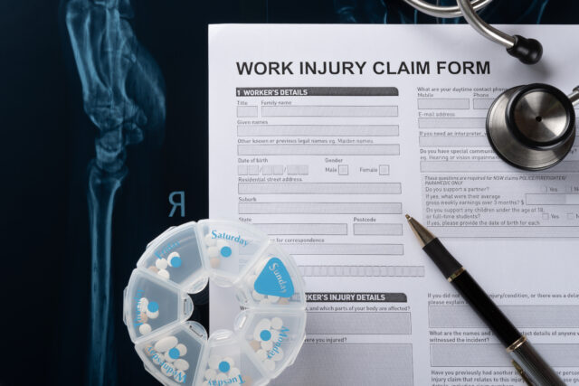 work injury claim form with stethoscope and box of pills on top of an X-ray film medical and insurance concept